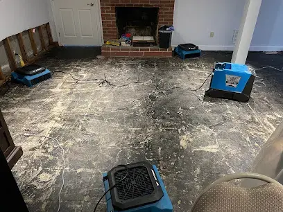 Brick fireplace behind a wet stained floor, with an air mover and dehumidifier running