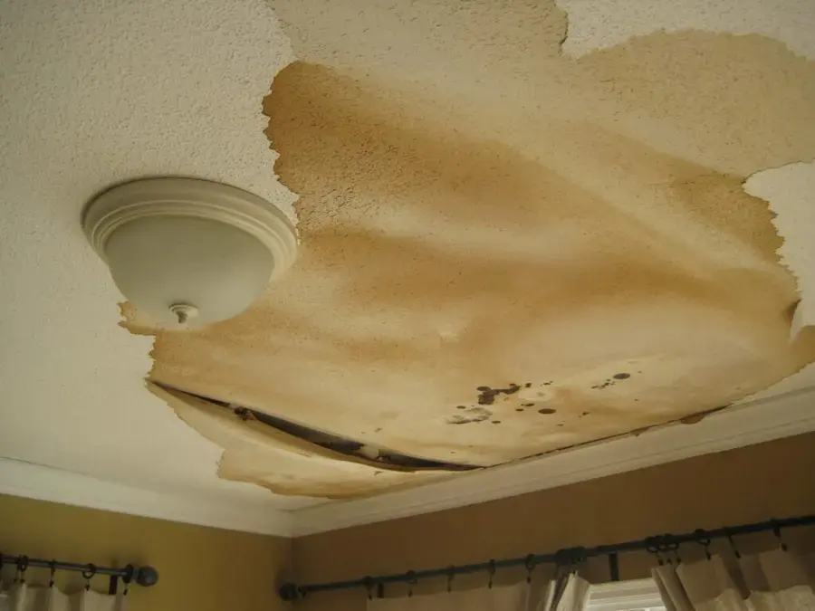 Water-stained ceiling sagging around a light fixture after a leak upstairs